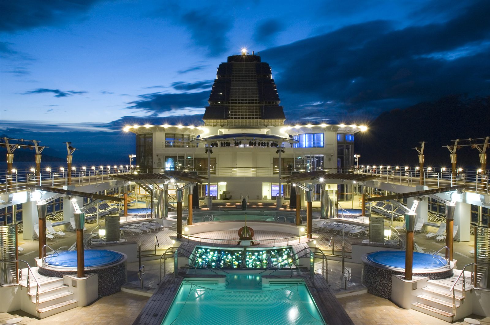 Cruise ship pool deck lit up at dusk, the reward side of learning how to sell cruises