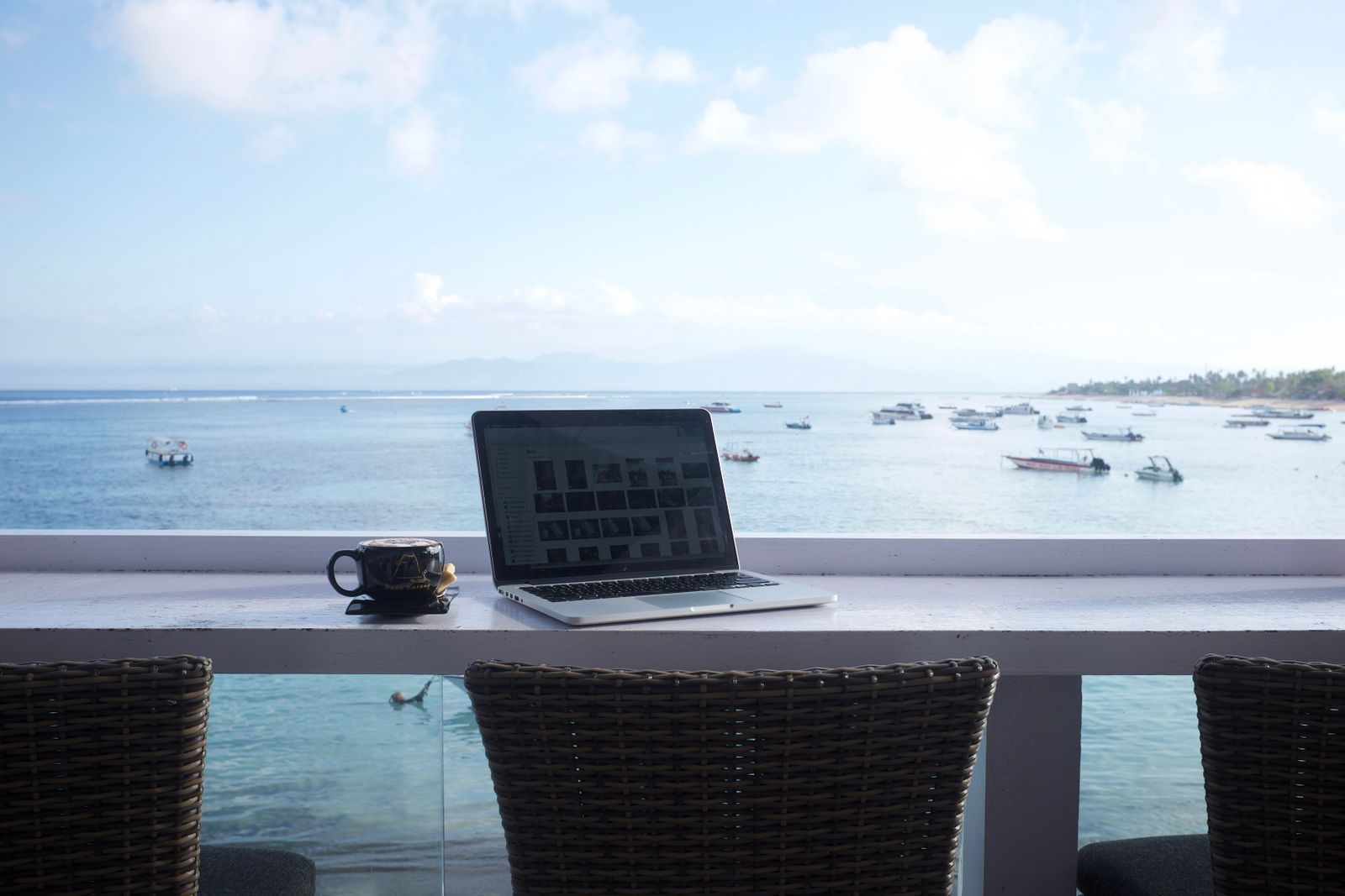 Laptop on a table facing a sea view with boats, a reminder of what fam rates for travel agents are for